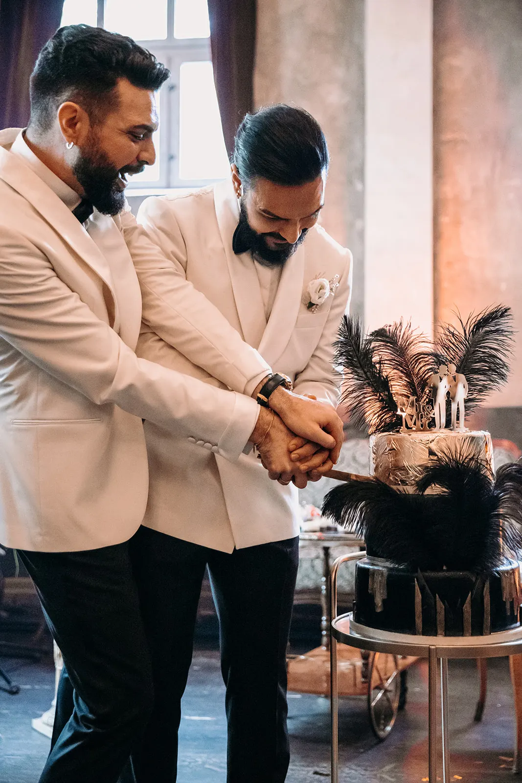 Zwei Bräutigame schneiden gemeinsam die Hochzeitstorte mit Mr-und-Mr-Topper an